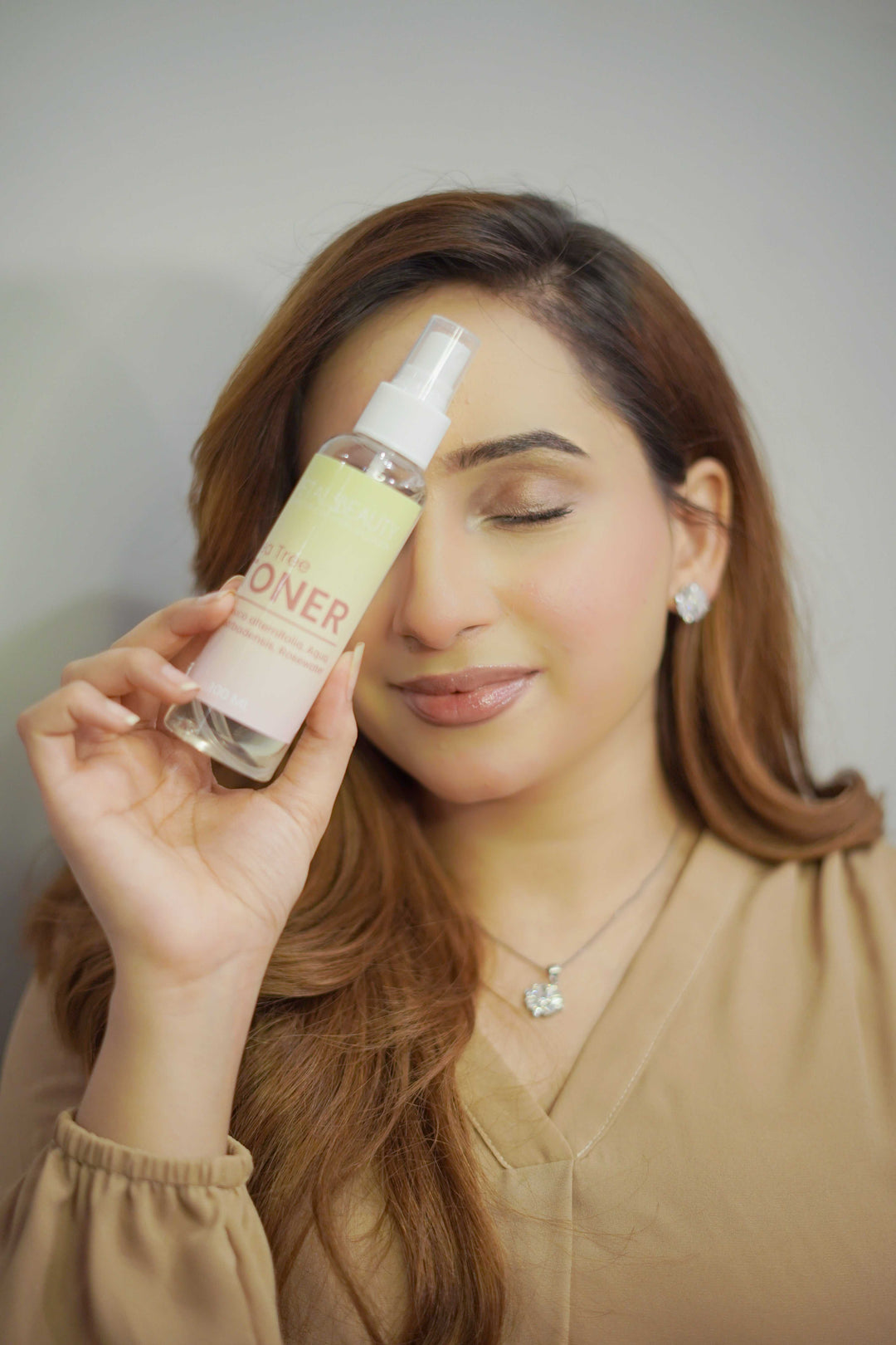 Woman holding a bottle of tea tree toner against a neutral background